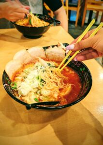 Close-up of Japanese ramen with noodles, pork, and vegetables in a black bowl.