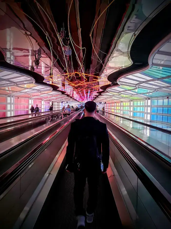 Man at Airport Walkway with bright colorful lights on wall of long hallway