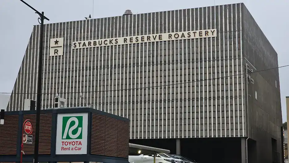 Large building with "Starbucks Reserve Roastery" text, gray vertical-striped design. Foreground shows "Toyota Rent a Car" sign. Overcast sky.
