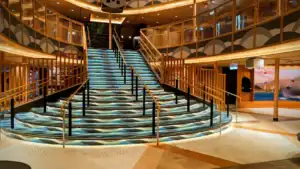 Elegant stairway with wavy blue-patterned carpet in a modern interior, surrounded by golden railings and warm lights. No people present.