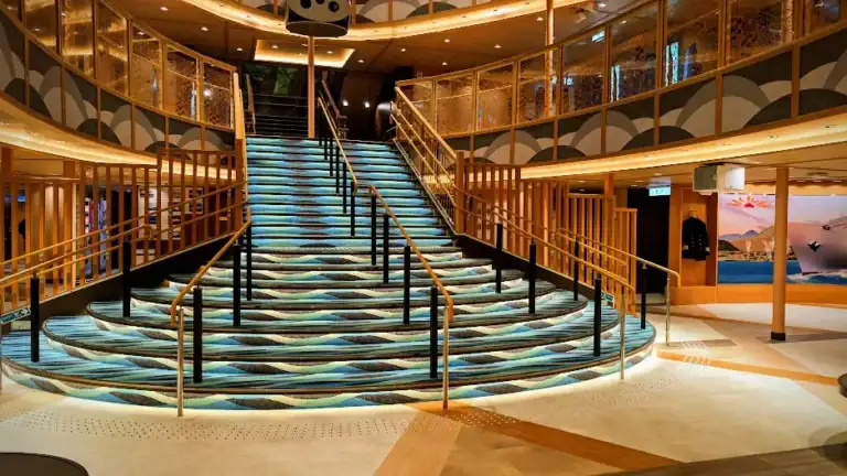 Elegant stairway with wavy blue-patterned carpet in a modern interior, surrounded by golden railings and warm lights. No people present.