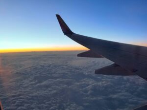 View of airplane wing over clouds during sunset for Japan travel.