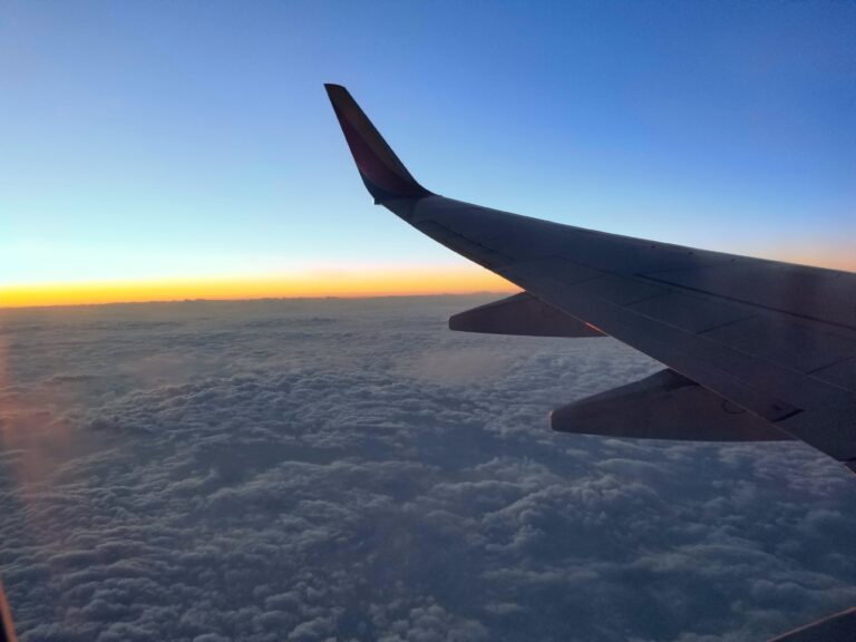 View of airplane wing over clouds during sunset for Japan travel.
