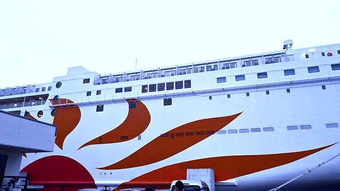 White ferry with a large red-orange sun design docked at a port. Clear sky in the background, creating a calm atmosphere. Sunflower Ferry Beppu Osaka