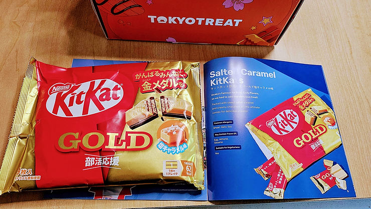 Tokyo Treat box with two KitKat Gold snack packages on a wooden table, red and gold, plus a blue booklet with product text