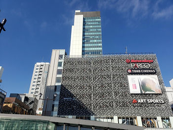 High-rise buildings under a clear blue sky. The main building displays signs for Matsuzakaya, PARCO, TOHO CINEMAS, and ART SPORTS.
