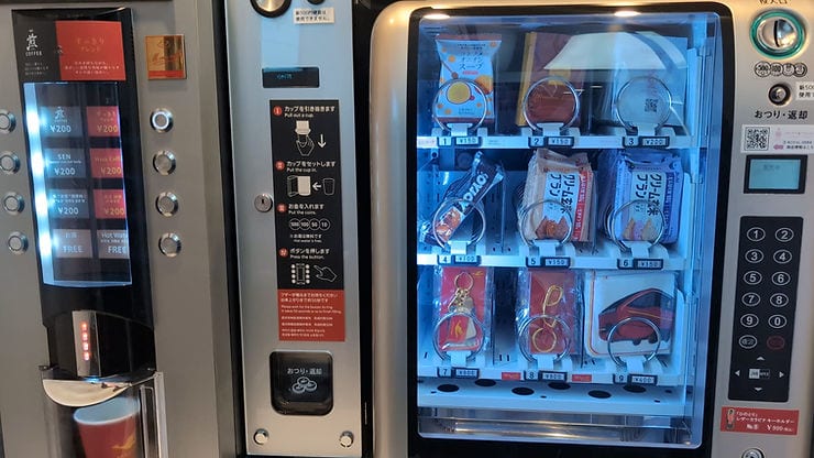 Coffee and snack vending machines side by side. Coffee options priced at ¥200, and various snacks visible under blue lighting.