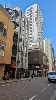 Urban street scene with people walking. Tall buildings, including Tosei Hotel, in background. Clear blue sky, various signs, parked van.