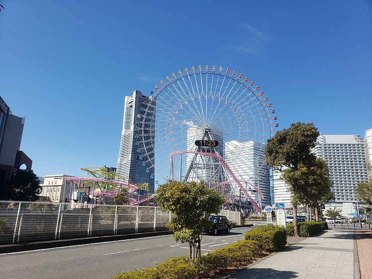 Giant ferris wheel and pink roller coaster in a city skyline under a clear blue sky, with a digital clock reading 11:23.