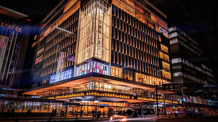 Building at night with bright lights and people in the street, one car passing 