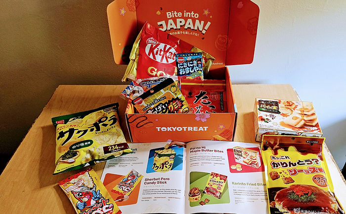 Orange TOKYOTREAT snack box with assorted Japanese candies and chips on a table, Japanese text visible