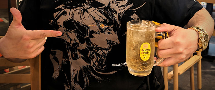 Man in black and beige graphic T-shirt holds a Suntory Whisky mug, pointing to the design. Gold watch visible, casual setting. whiskey highball