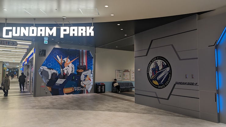 Gundam Park with bold sign, colorful robot mural on wall. Person seated, corridor to the left. Modern, clean atmosphere.