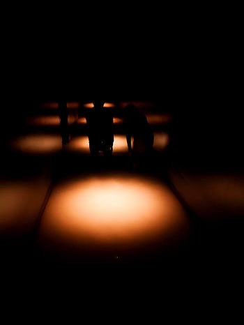 Silhouettes of two people kneeling on a path illuminated by warm, circular lights. Dark, moody atmosphere with a focus on light patterns.