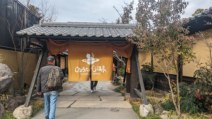 Traditional Japanese onsen entrance with yellow noren and wooden gate.