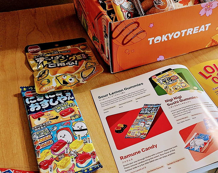 TokyoTreat snack box with Japanese candy packets and a booklet showing Sour Lemon Gummies, Nigi Nigi Sushi Gummies, and Ramune Candy.