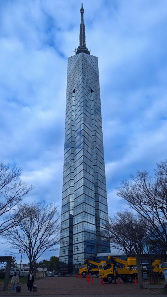 Tall Fukuoka Tower against cloudy sky in Japan.