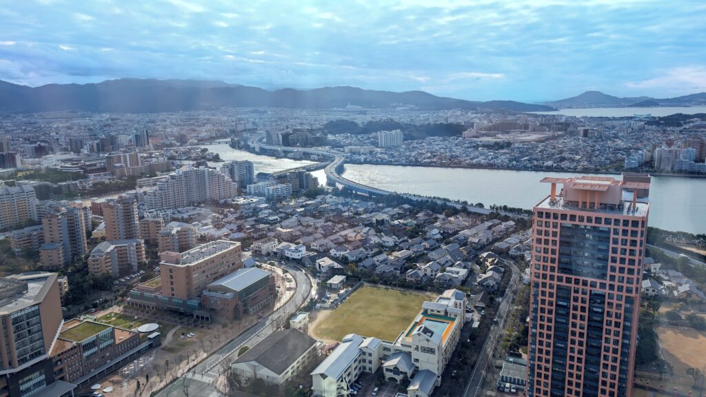 Aerial view of Fukuoka city with river and mountains in the background.