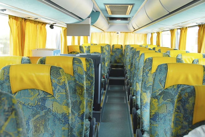 Empty bus interior with patterned blue and yellow seats and yellow curtains. Bright daylight filters in through the windows, creating a calm mood.