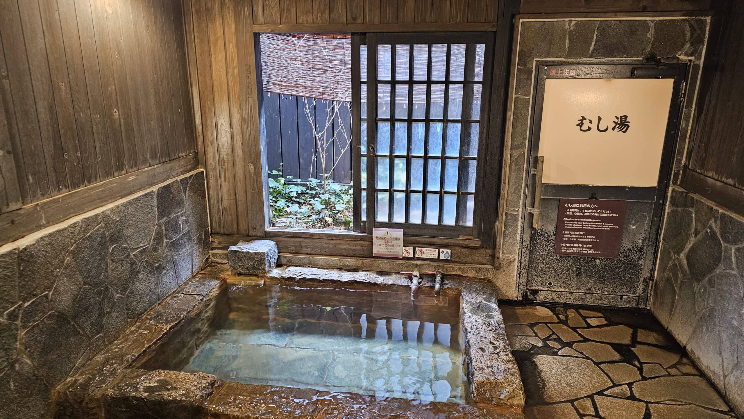 Traditional indoor private hot spring stone onsen bath with wooden walls and steam room door at Hyotan Onsen in Beppu Kyushu Japan