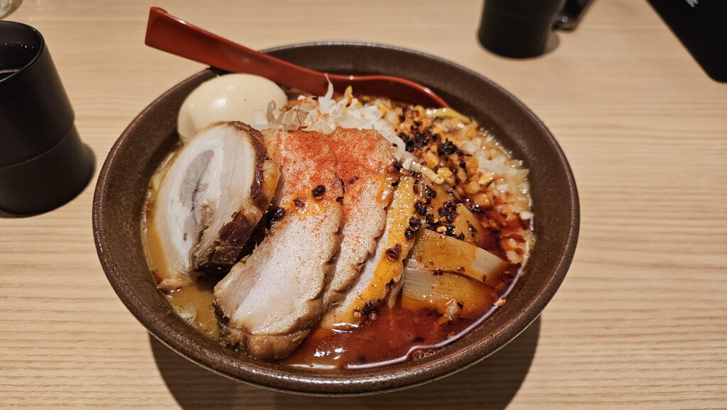 A steaming, authentic bowl of Japanese ramen topped with sliced chashu pork, a soft-boiled egg, nori seaweed, and green onions.